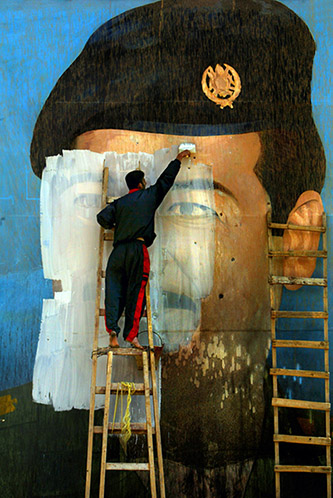 Carolyn Cole, Une photo de Saddam Hussein, criblée d’impacts de balles, est recouverte de peinture par Salem Yuel. Les symboles des dirigeants politiques ont disparu de Bagdad peu après la prise de la ville par les troupes américaines. Bagdad, Irak, avril 2003. © Carolyn Cole / Los Angeles Times.