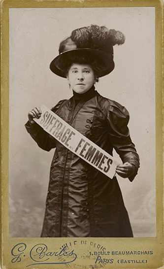 Charles, Hubertine Auclert tenant une banderole concernant le suffrage des femmes, 1910. Bibliothèque Marguerite Durand.