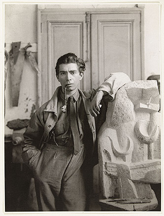 Marc Vaux, Zadkine dans son atelier de la rue Rousselet, accoudé à  Formes féminines, Vers 1920. Épreuve gélatino-argentique, 24 x 17,7 cm. Paris, musée Zadkine. © Adagp, Paris 2022.