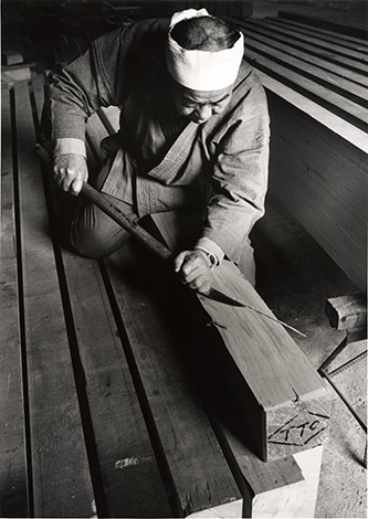 Le maître charpentier Tsunekazu Nishioka aplanissant une surface de bois avec un yari-ganna. © Takenaka Carpentry Tools Museum.