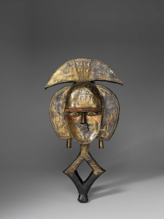 Statuette de gardien de reliquaire Mbulu-ngulu. N° inventaire 71.1941.13.1. Figure humaine stylisée constituée d'un janus sur une base losangique dont la partie supérieure est recouverte de cuivre et décorée d'un motif de triangles guillochés opposés par la pointe. L'un des visage possède un front bombé, l'autre est concave, surmontés d'une coiffure stylisée, formée par un croissant avec au centre un motif de triangles opposés. De chaque côtés du visage, deux croissants, à base coupée, terminés chacun par un pendant. Nom de l'exposition, Les forêts natales, Arts de l'Afrique Équatoriale atlantique Statue de gardien de reliquaire. 19e siècle. Bois : Emien ou Alstonia, Famille : APOCYNACEAE, Espèce : Alstonia boonei laiton jaune, laiton jaune au plomb, cuivre au plomb et fer. 63 x 30,5 x 10,5 cm, 4 242 g. Haut-Ogooué Afrique Gabon Obamba Afrique centrale. © musée du quai Branly - Jacques Chirac, photo Patrick Gries, Valérie Torre.